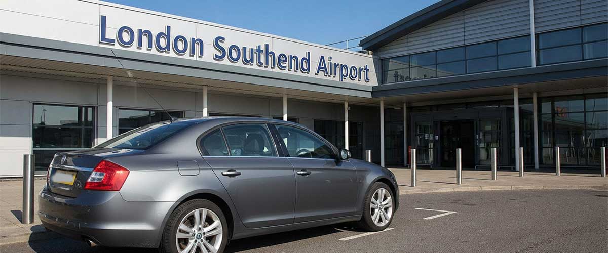 Silver taxi representing Ashford Infinity Cabs, parked directly outside the main London Southend Airport terminal building. Dependable local airport taxi service.